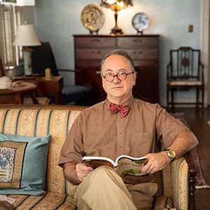 Robert Boggs holding book open while sitting on couch.