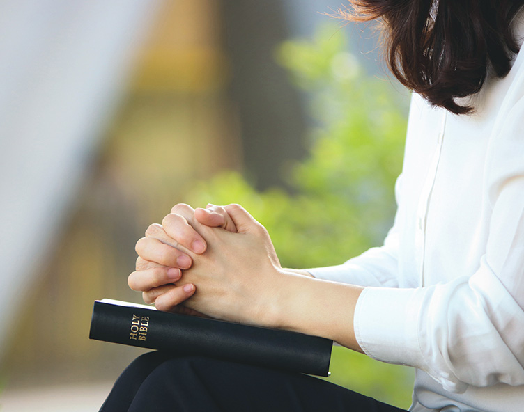 girl with hands folded over bible in park