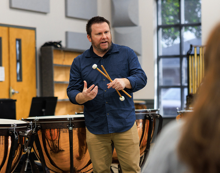 professor giving a percusssion lesson near a set of drums